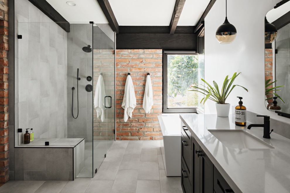 This is an example of a master bathroom in Phoenix with shaker cabinets, black cabinets, a freestanding tub, a corner shower, porcelain tile, porcelain floors, engineered quartz benchtops, grey floor, a hinged shower door, grey benchtops, gray tile and an undermount sink.
