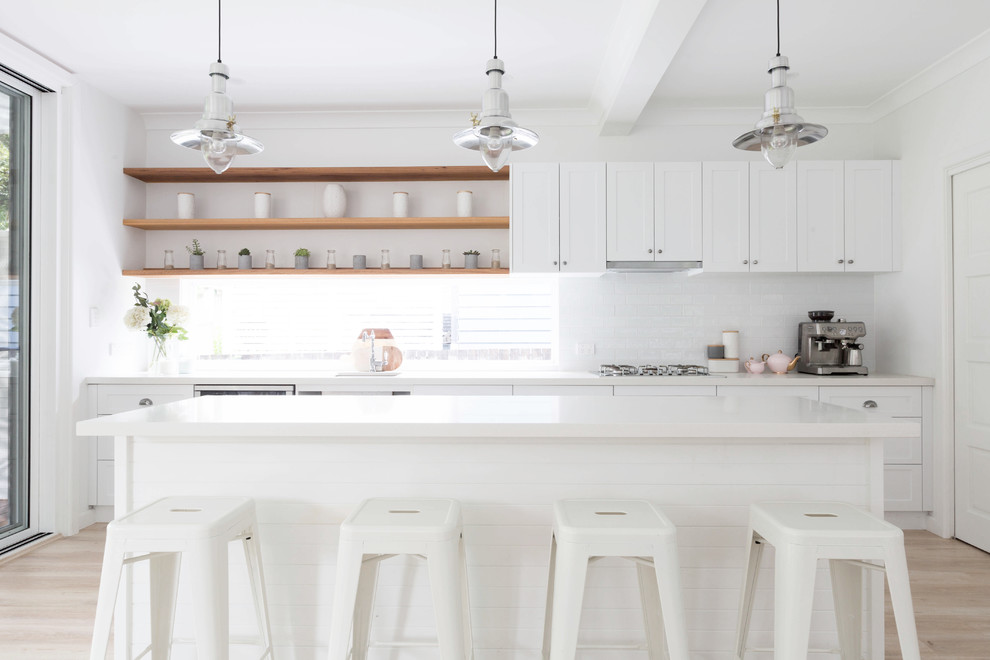 Inspiration for a mid-sized beach style single-wall kitchen in Sydney with an undermount sink, shaker cabinets, white cabinets, quartz benchtops, white splashback, subway tile splashback, stainless steel appliances, laminate floors, with island, beige floor and white benchtop.