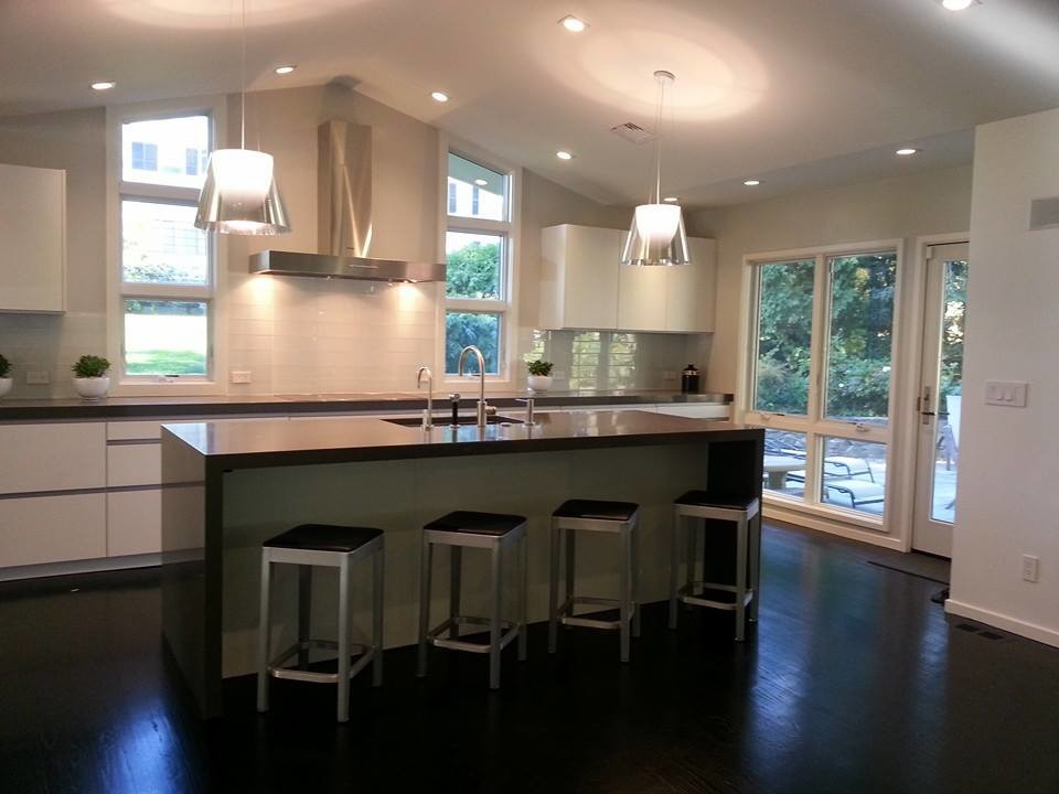 Open concept kitchen - mid-sized transitional single-wall medium tone wood floor open concept kitchen idea in Boston with a drop-in sink, flat-panel cabinets, white cabinets, granite countertops, white backsplash, stone tile backsplash, stainless steel appliances and an island
