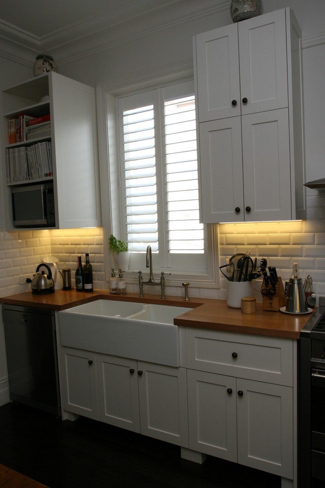This is an example of a mid-sized traditional u-shaped eat-in kitchen in Sydney with a double-bowl sink, shaker cabinets, white cabinets, wood benchtops, white splashback, ceramic splashback, stainless steel appliances and dark hardwood floors.