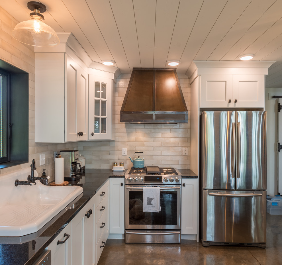 Example of a mid-sized mountain style l-shaped concrete floor and gray floor open concept kitchen design in Minneapolis with a drop-in sink, shaker cabinets, white cabinets, solid surface countertops, beige backsplash, subway tile backsplash, stainless steel appliances, an island and black countertops