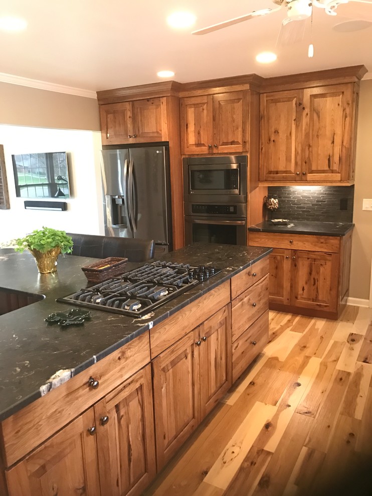 Inspiration for a large country l-shaped eat-in kitchen in Other with an undermount sink, raised-panel cabinets, medium wood cabinets, granite benchtops, grey splashback, ceramic splashback, stainless steel appliances, light hardwood floors, with island and beige floor.