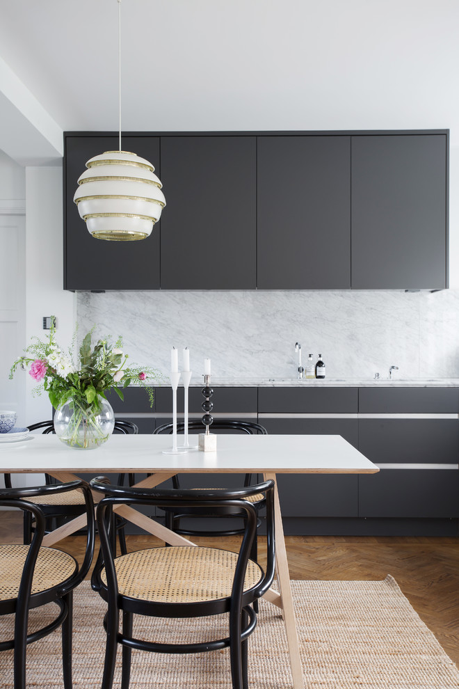 This is an example of a mid-sized scandinavian single-wall eat-in kitchen in Stockholm with flat-panel cabinets, black cabinets, white splashback, stone slab splashback, medium hardwood floors, marble benchtops and no island.