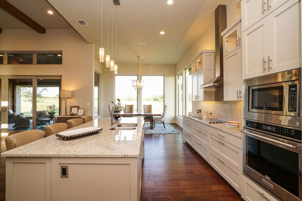 Large contemporary single-wall eat-in kitchen in Austin with a double-bowl sink, shaker cabinets, white cabinets, granite benchtops, white splashback, stone tile splashback, stainless steel appliances, medium hardwood floors and with island.