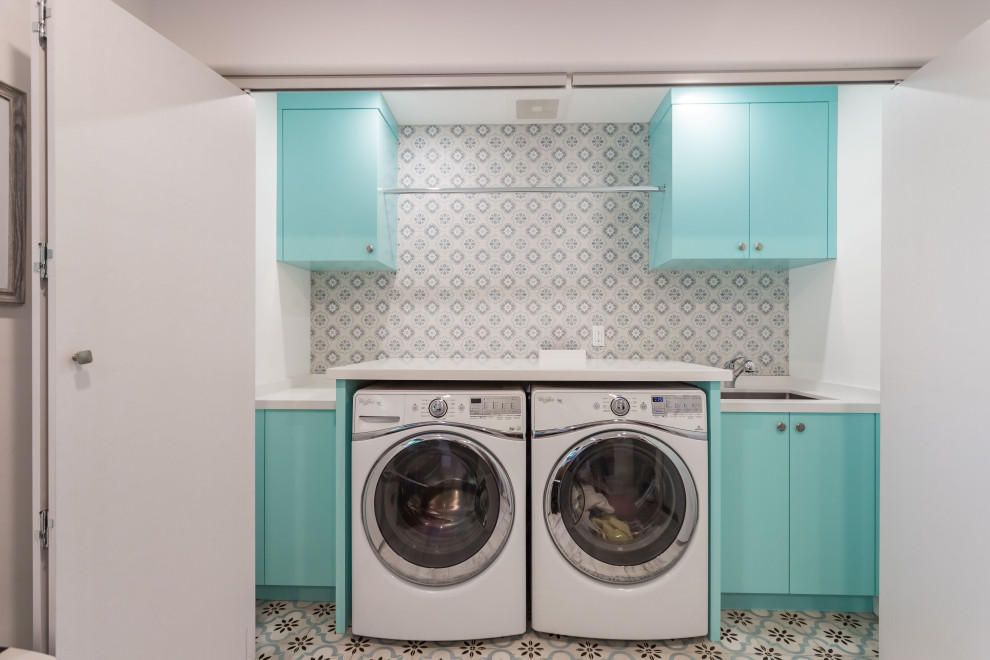 Inspiration for a small single-wall laundry cupboard in Los Angeles with a drop-in sink, flat-panel cabinets, turquoise cabinets, wood benchtops, multi-coloured splashback, ceramic splashback, white walls, ceramic floors, a side-by-side washer and dryer, multi-coloured floor, white benchtop, vaulted and panelled walls.