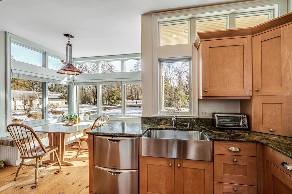 This is an example of a mid-sized contemporary u-shaped open plan kitchen in Boston with a farmhouse sink, shaker cabinets, light wood cabinets, granite benchtops, black splashback, stone slab splashback, stainless steel appliances, light hardwood floors, a peninsula and yellow floor.