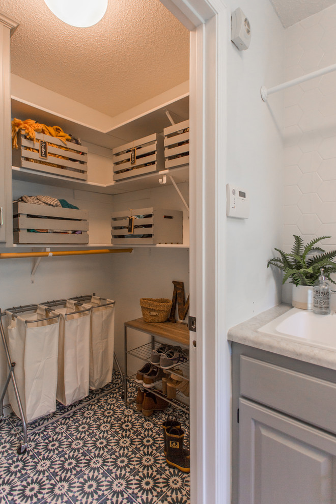 Photo of a large transitional utility room in Minneapolis with concrete floors, a side-by-side washer and dryer, blue floor, a drop-in sink, raised-panel cabinets, grey cabinets and yellow walls.