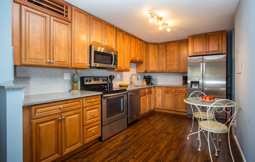 Photo of a mid-sized transitional l-shaped eat-in kitchen in DC Metro with an undermount sink, raised-panel cabinets, medium wood cabinets, quartz benchtops, grey splashback, stone tile splashback, stainless steel appliances, dark hardwood floors, with island and brown floor.