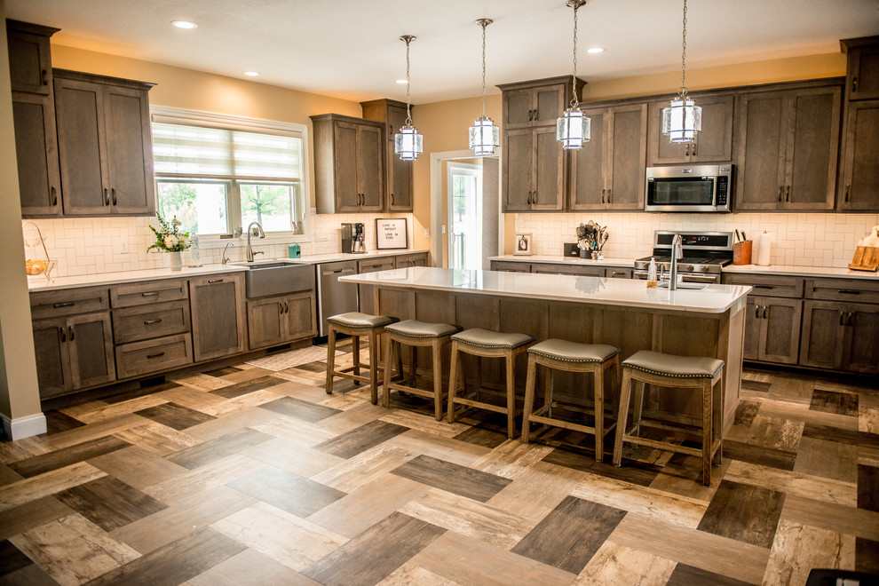 Open concept kitchen - large transitional l-shaped vinyl floor and multicolored floor open concept kitchen idea with a farmhouse sink, shaker cabinets, gray cabinets, quartz countertops, white backsplash, subway tile backsplash, stainless steel appliances, an island and white countertops
