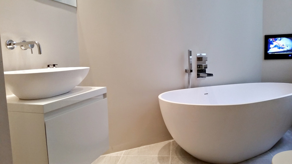 Inspiration for a large contemporary bathroom in London with a trough sink, white cabinets, solid surface benchtops, a freestanding tub, gray tile, ceramic tile, grey walls and porcelain floors.