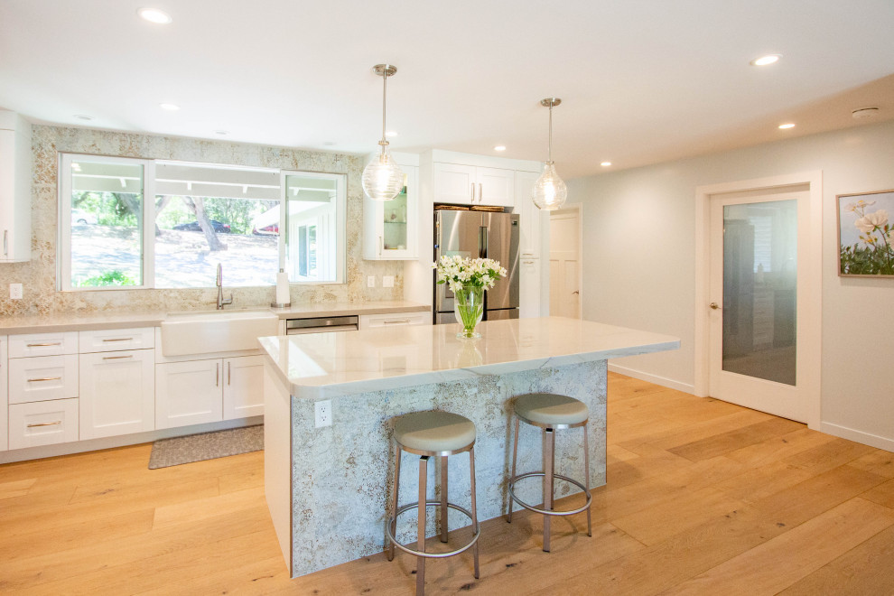 Inspiration for a transitional l-shaped light wood floor and brown floor eat-in kitchen remodel with a farmhouse sink, shaker cabinets, white cabinets, quartz countertops, porcelain backsplash, stainless steel appliances and an island