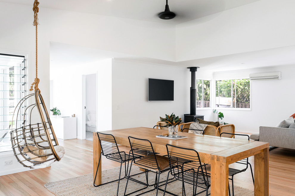 Photo of a contemporary open plan dining in Brisbane with white walls, light hardwood floors and a wood stove.