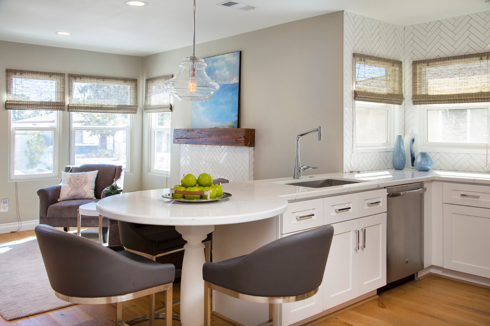 Inspiration for a small transitional u-shaped medium tone wood floor open concept kitchen remodel in San Diego with an undermount sink, shaker cabinets, white cabinets, quartz countertops, white backsplash, ceramic backsplash, stainless steel appliances and a peninsula