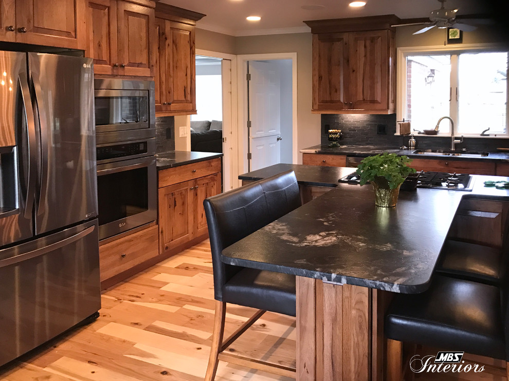 Eat-in kitchen - large rustic l-shaped light wood floor and beige floor eat-in kitchen idea with an undermount sink, raised-panel cabinets, medium tone wood cabinets, granite countertops, gray backsplash, ceramic backsplash, stainless steel appliances and an island