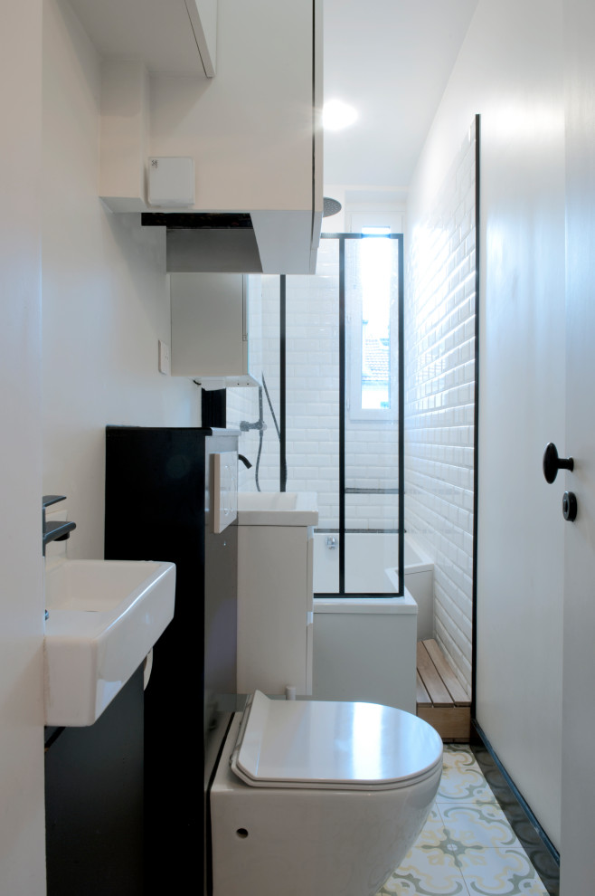 Стильный дизайн: маленькая, узкая и длинная ванная комната в современном стиле с фасадами с декоративным кантом, белыми фасадами, ванной в нише, душем над ванной, инсталляцией, белой плиткой, плиткой кабанчик, белыми стенами, полом из цементной плитки, душевой кабиной, консольной раковиной, столешницей из искусственного камня, разноцветным полом, душем с распашными дверями, белой столешницей, тумбой под одну раковину и подвесной тумбой для на участке и в саду - последний тренд