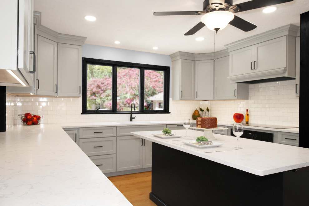 Example of a large transitional u-shaped light wood floor and brown floor enclosed kitchen design in Boston with a double-bowl sink, shaker cabinets, gray cabinets, quartz countertops, white backsplash, porcelain backsplash, black appliances, an island and white countertops