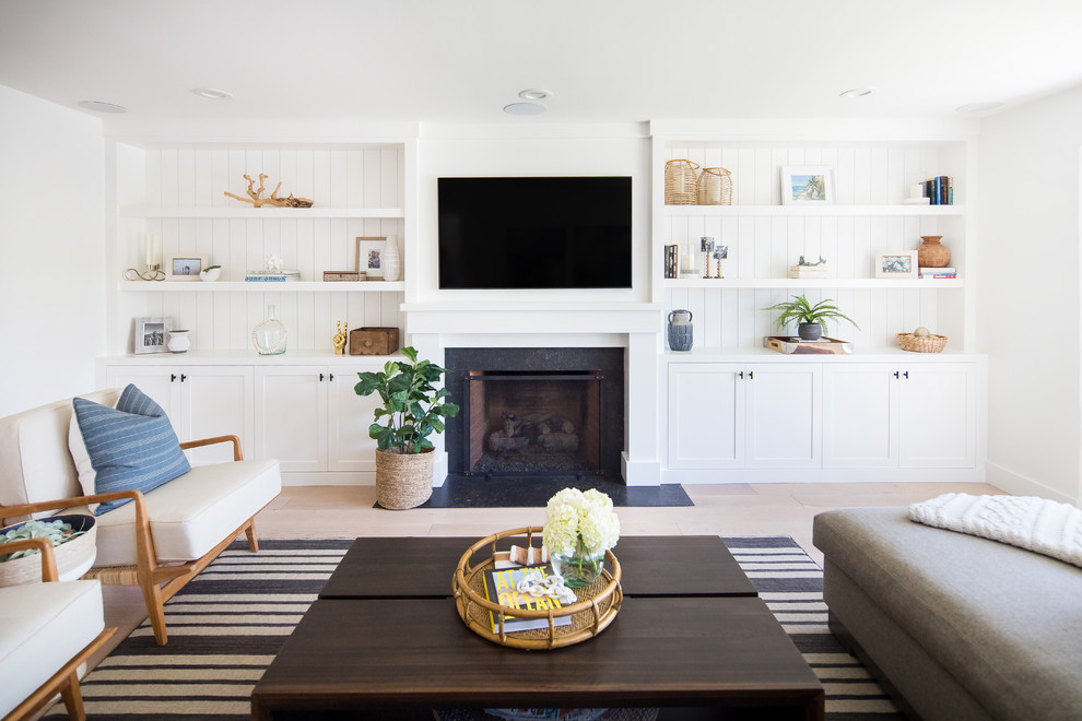 Inspiration for a beach style enclosed family room in Orange County with white walls, light hardwood floors, a standard fireplace, a stone fireplace surround and a built-in media wall.