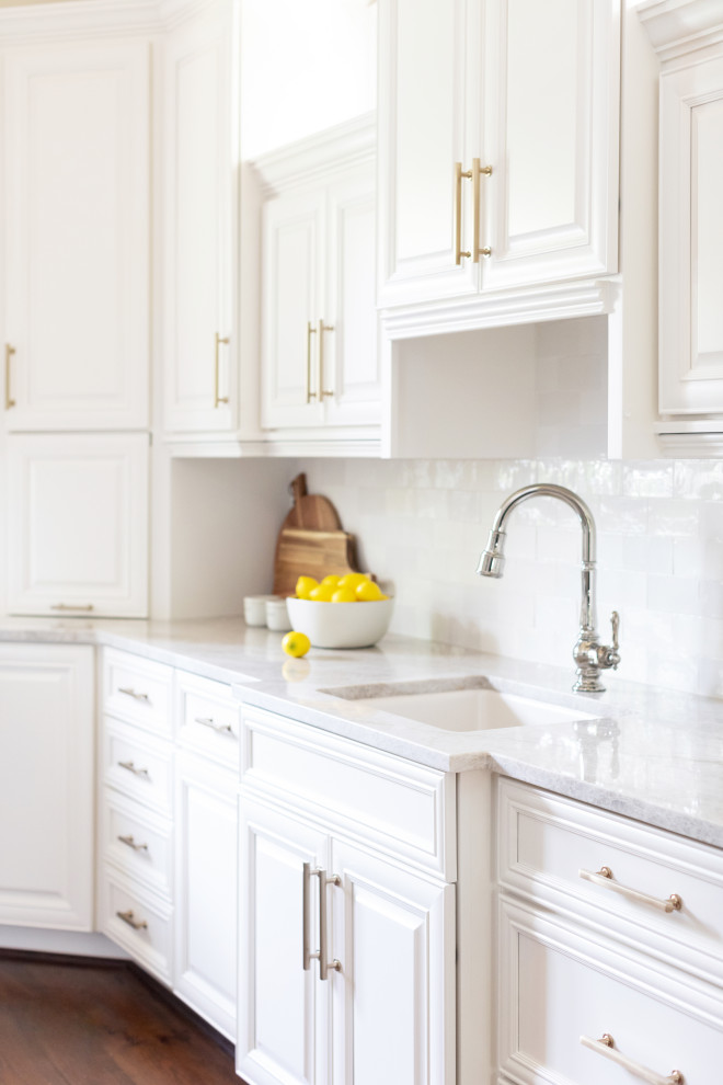 Foto på ett stort vintage vit kök, med en enkel diskho, luckor med upphöjd panel, vita skåp, bänkskiva i kvartsit, vitt stänkskydd, stänkskydd i keramik, rostfria vitvaror, mörkt trägolv, en köksö och brunt golv