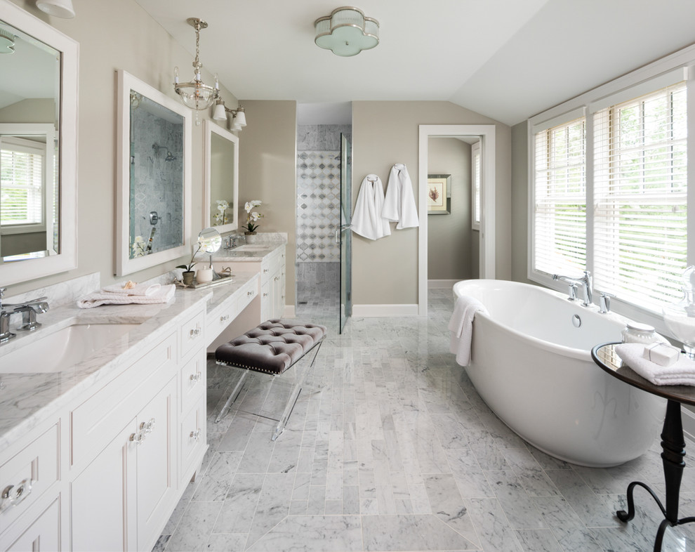 Photo of a beach style master bathroom in Minneapolis with recessed-panel cabinets, white cabinets, a freestanding tub, gray tile, multi-coloured tile, beige walls, an undermount sink, grey floor and a hinged shower door.