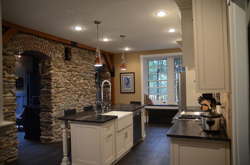Design ideas for a mid-sized transitional l-shaped open plan kitchen in Philadelphia with a farmhouse sink, shaker cabinets, white cabinets, soapstone benchtops, beige splashback, stone tile splashback, stainless steel appliances, dark hardwood floors and with island.