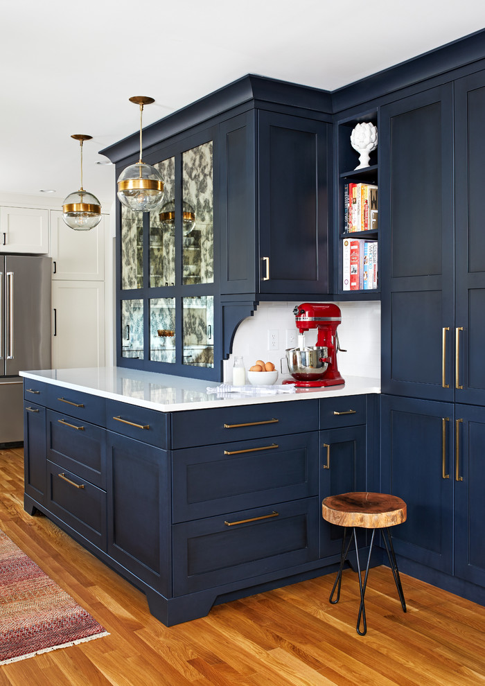 Design ideas for a mid-sized transitional kitchen in DC Metro with a single-bowl sink, blue cabinets, quartz benchtops, white splashback, subway tile splashback, stainless steel appliances, medium hardwood floors, a peninsula, brown floor, white benchtop and shaker cabinets.