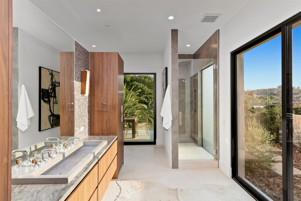 Photo of a contemporary bathroom in San Diego with flat-panel cabinets, medium wood cabinets, an alcove shower, gray tile, white walls, a trough sink, beige floor, a hinged shower door, grey benchtops, a double vanity and a floating vanity.
