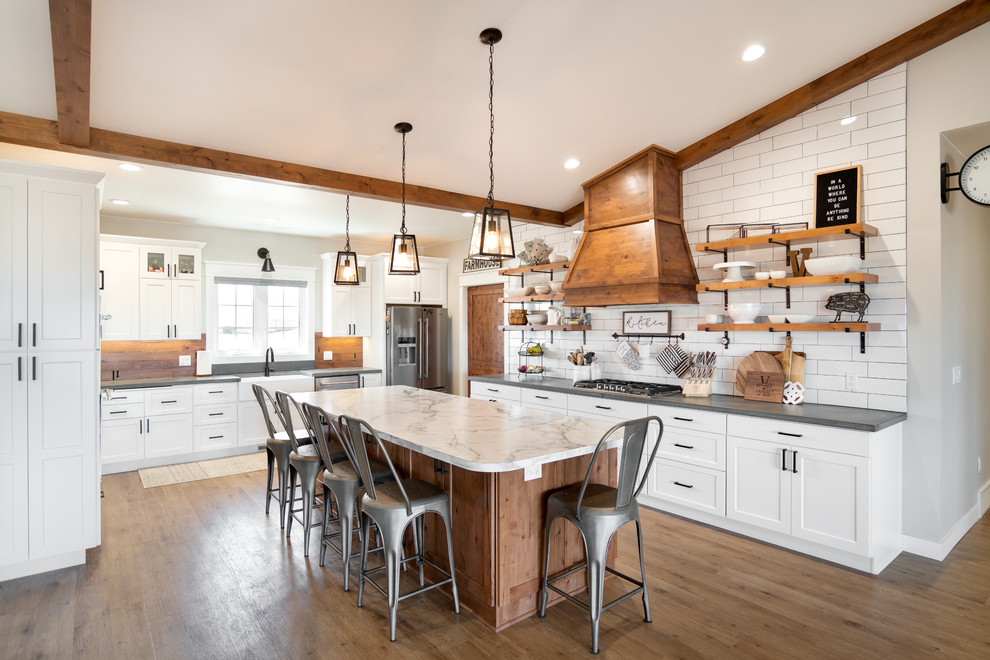 Design ideas for a large country l-shaped eat-in kitchen in Other with a farmhouse sink, shaker cabinets, white cabinets, laminate benchtops, stainless steel appliances, medium hardwood floors, with island, brown floor, white benchtop and white splashback.