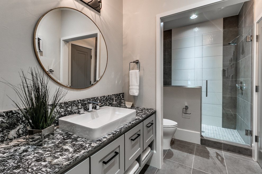 Photo of a mid-sized transitional 3/4 bathroom in Oklahoma City with shaker cabinets, grey cabinets, an alcove shower, a one-piece toilet, black and white tile, porcelain tile, grey walls, porcelain floors, a vessel sink, marble benchtops, grey floor and a hinged shower door.