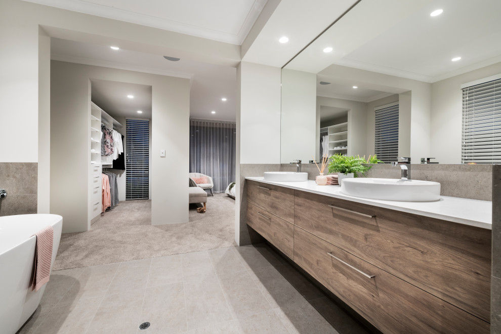 This is an example of a large contemporary master bathroom in Perth with flat-panel cabinets, medium wood cabinets, a freestanding tub, gray tile, white walls, porcelain floors, a vessel sink, grey floor and white benchtops.
