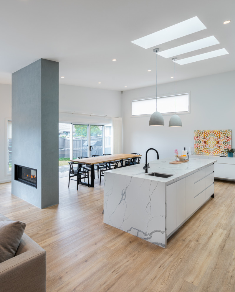 Large modern kitchen/diner in Sydney with a single-bowl sink, flat-panel cabinets, white cabinets, engineered stone countertops, white splashback, engineered quartz splashback, black appliances, vinyl flooring, an island, brown floors, white worktops and a vaulted ceiling.