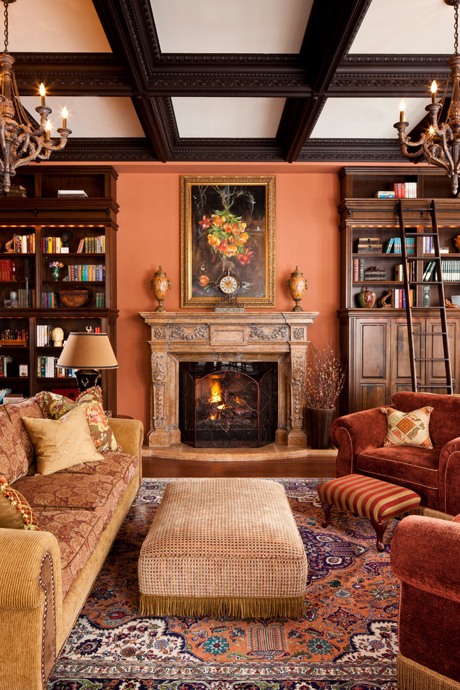 This is an example of a traditional living room in Toronto with a library, orange walls and a standard fireplace.