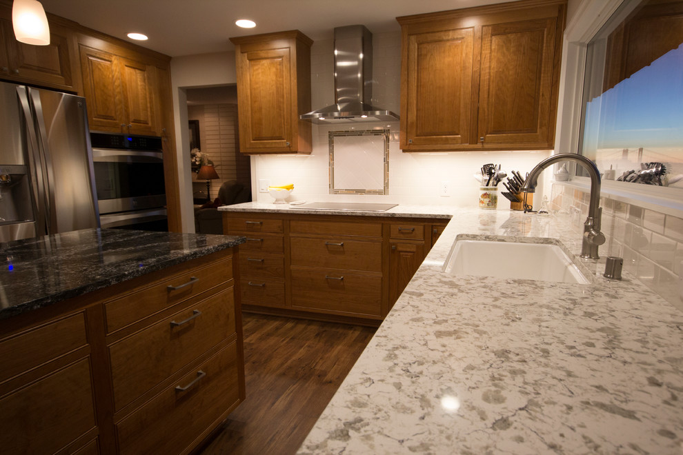 Photo of a mid-sized traditional l-shaped separate kitchen in Seattle with an undermount sink, raised-panel cabinets, medium wood cabinets, quartz benchtops, white splashback, subway tile splashback, stainless steel appliances, medium hardwood floors and with island.