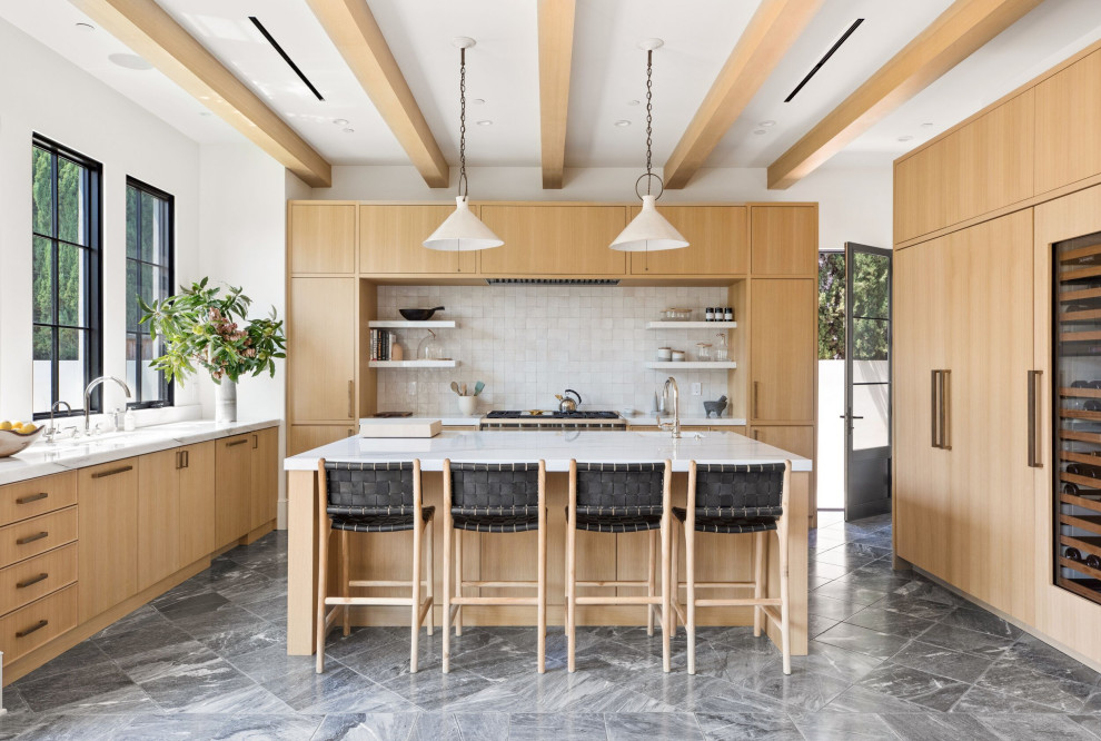 Large transitional l-shaped open plan kitchen in Los Angeles with an undermount sink, flat-panel cabinets, light wood cabinets, marble benchtops, white splashback, mosaic tile splashback, panelled appliances, marble floors, with island, black floor, white benchtop and exposed beam.