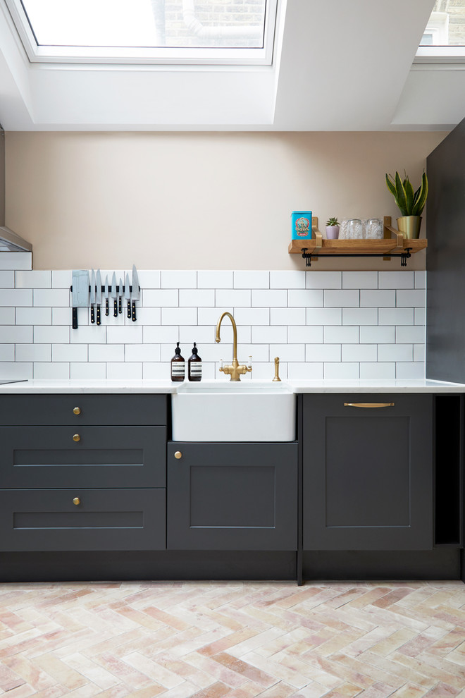 Photo of a medium sized modern open plan kitchen in London with a belfast sink, flat-panel cabinets, grey cabinets, composite countertops, white splashback, ceramic splashback, stainless steel appliances, ceramic flooring, an island, orange floors and white worktops.