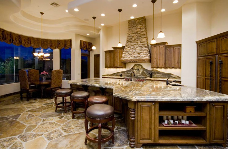 Inspiration for a large mediterranean galley eat-in kitchen in Phoenix with raised-panel cabinets, medium wood cabinets, granite benchtops, beige splashback, stone tile splashback, stainless steel appliances, travertine floors and with island.