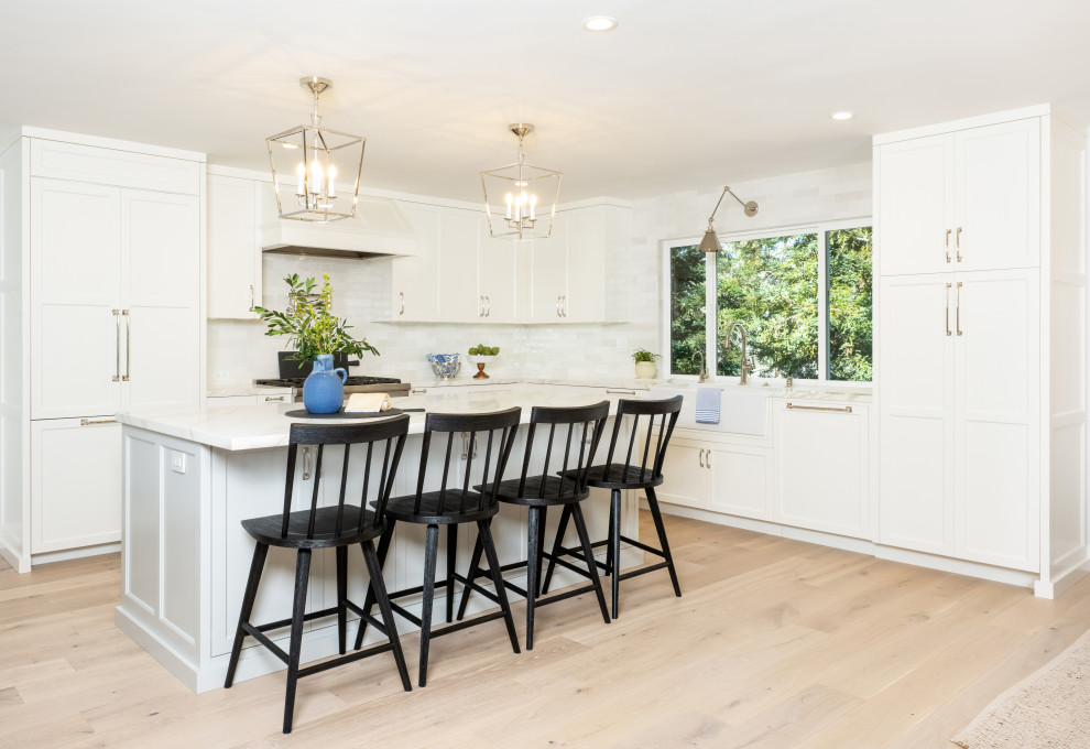 Photo of a large farmhouse l-shaped kitchen/diner in San Francisco with a belfast sink, shaker cabinets, white cabinets, engineered stone countertops, white splashback, metro tiled splashback, an island, brown floors, white worktops, integrated appliances and light hardwood flooring.