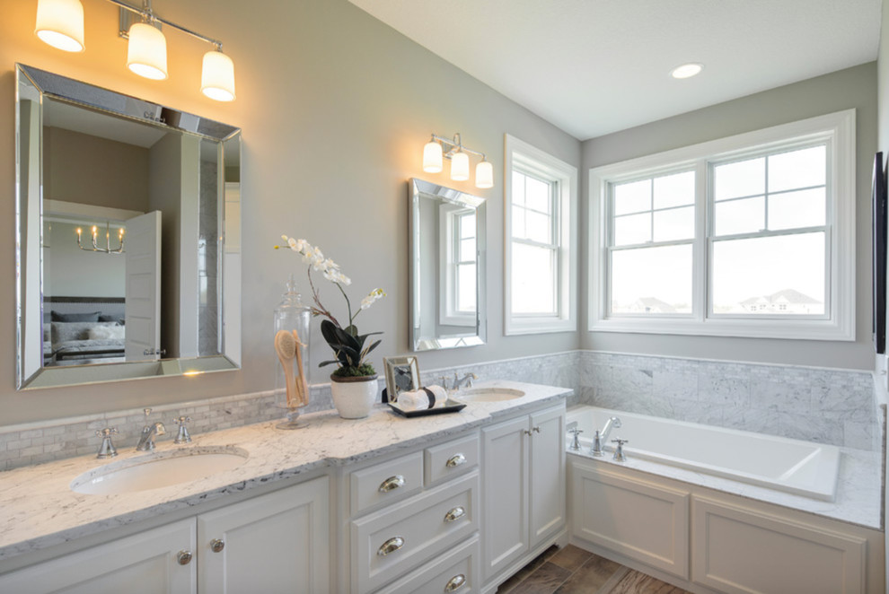 Large transitional master white tile and marble tile medium tone wood floor and brown floor drop-in bathtub photo with recessed-panel cabinets, white cabinets, beige walls, a drop-in sink and marble countertops