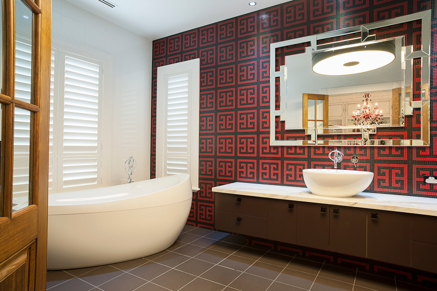 This is an example of an expansive eclectic master bathroom in Melbourne with a vessel sink, furniture-like cabinets, brown cabinets, marble benchtops, a freestanding tub, a shower/bathtub combo, a wall-mount toilet, red tile, glass tile, multi-coloured walls and porcelain floors.