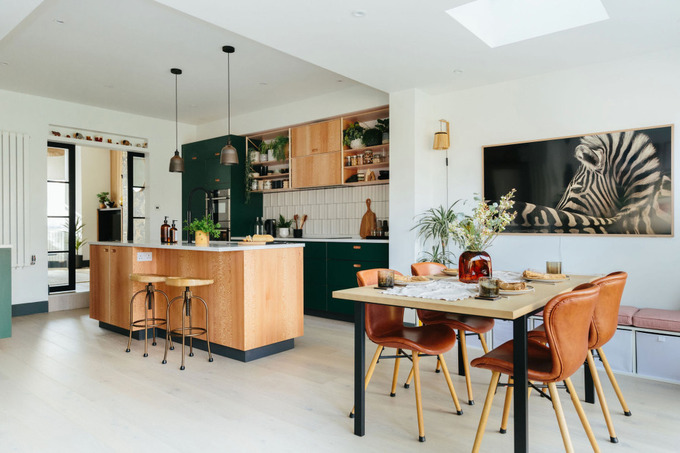 Стильный дизайн: кухня-гостиная среднего размера с монолитной мойкой, плоскими фасадами, зелеными фасадами, белым фартуком, фартуком из керамической плитки, цветной техникой, полом из ламината, островом и серым полом - последний тренд