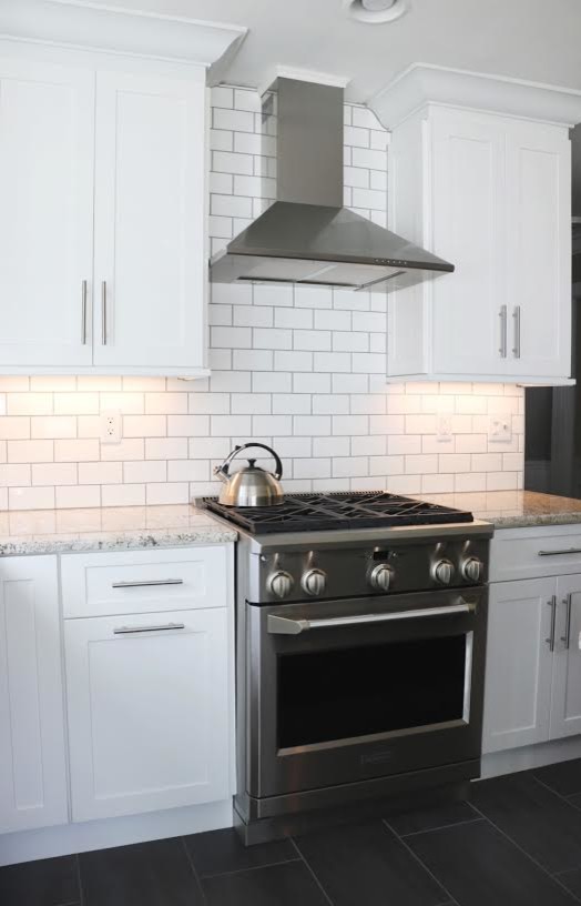 Mid-sized transitional u-shaped eat-in kitchen in New York with shaker cabinets, white cabinets, granite benchtops, white splashback, with island, an undermount sink, subway tile splashback, stainless steel appliances, porcelain floors and black floor.