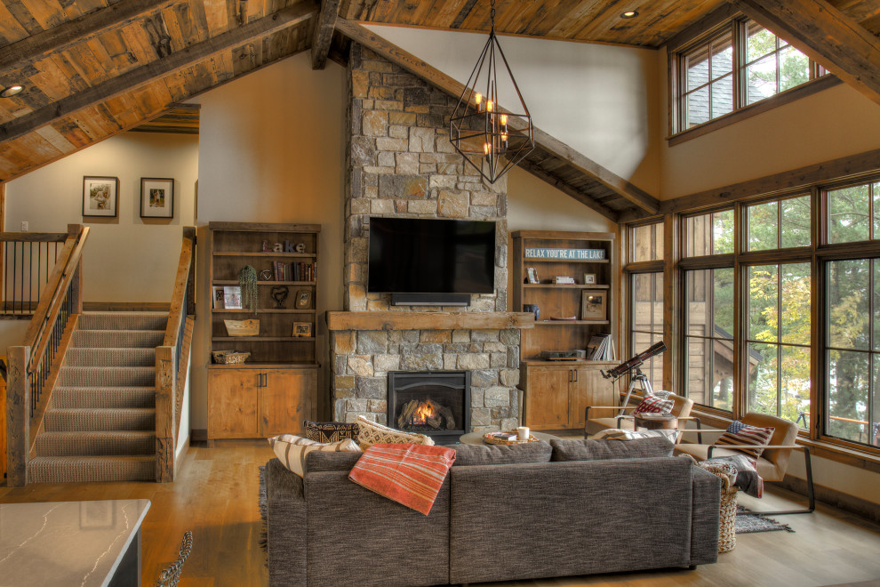 Large traditional open plan games room in Minneapolis with beige walls, light hardwood flooring, a standard fireplace, a stone fireplace surround, a wall mounted tv, brown floors and a wood ceiling.