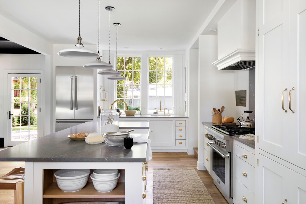 Lantlig inredning av ett mellanstort grå grått kök, med en rustik diskho, skåp i shakerstil, vita skåp, bänkskiva i kvarts, vitt stänkskydd, rostfria vitvaror, ljust trägolv, en köksö och brunt golv