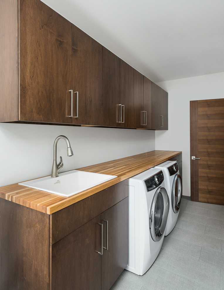 Mid-sized contemporary single-wall dedicated laundry room in Chicago with flat-panel cabinets, porcelain floors, a side-by-side washer and dryer, grey floor, a drop-in sink, medium wood cabinets, wood benchtops, white walls and brown benchtop.