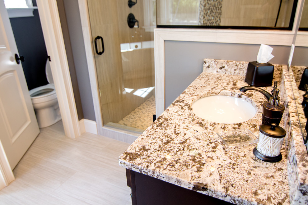 Inspiration for a large transitional master beige tile and ceramic tile ceramic tile freestanding bathtub remodel in Providence with an undermount sink, raised-panel cabinets, dark wood cabinets, granite countertops, a two-piece toilet and gray walls