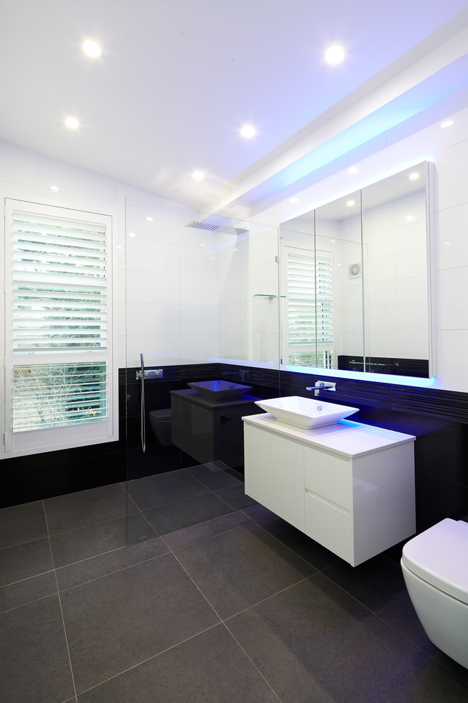 Inspiration for a small contemporary 3/4 bathroom in Sydney with a vessel sink, flat-panel cabinets, white cabinets, a curbless shower, a wall-mount toilet, black tile, ceramic tile, white walls and ceramic floors.