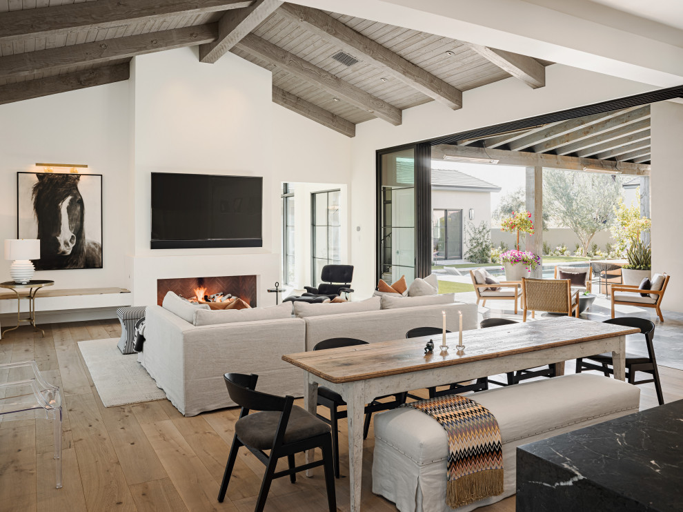 This is an example of a modern open plan dining in Phoenix with white walls, light hardwood floors, a ribbon fireplace, a plaster fireplace surround, beige floor and exposed beam.