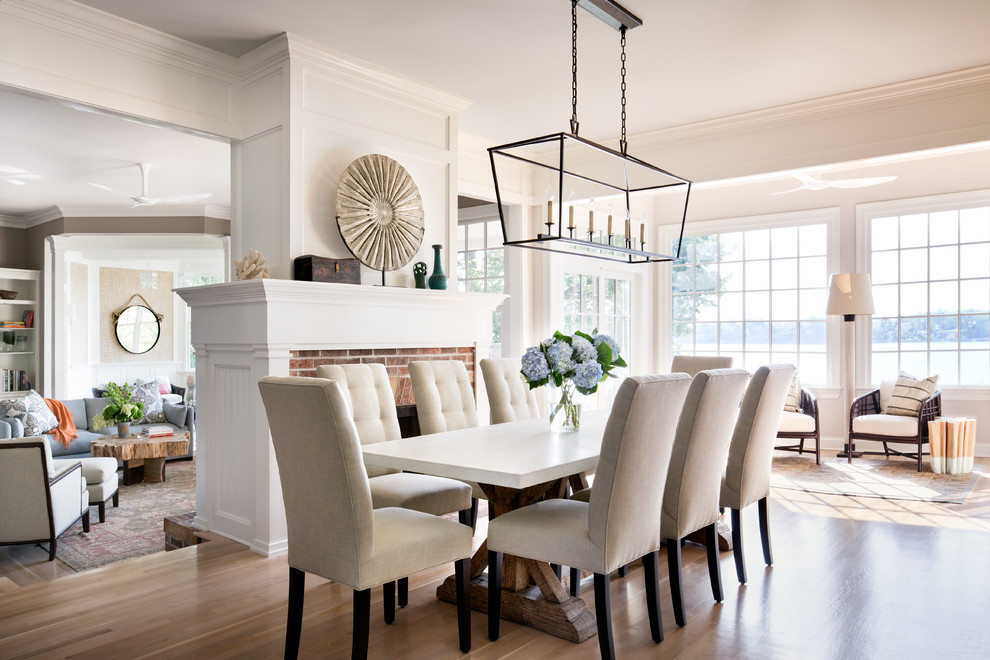 Inspiration for a large transitional open plan dining in New York with white walls, light hardwood floors, a brick fireplace surround and a standard fireplace.