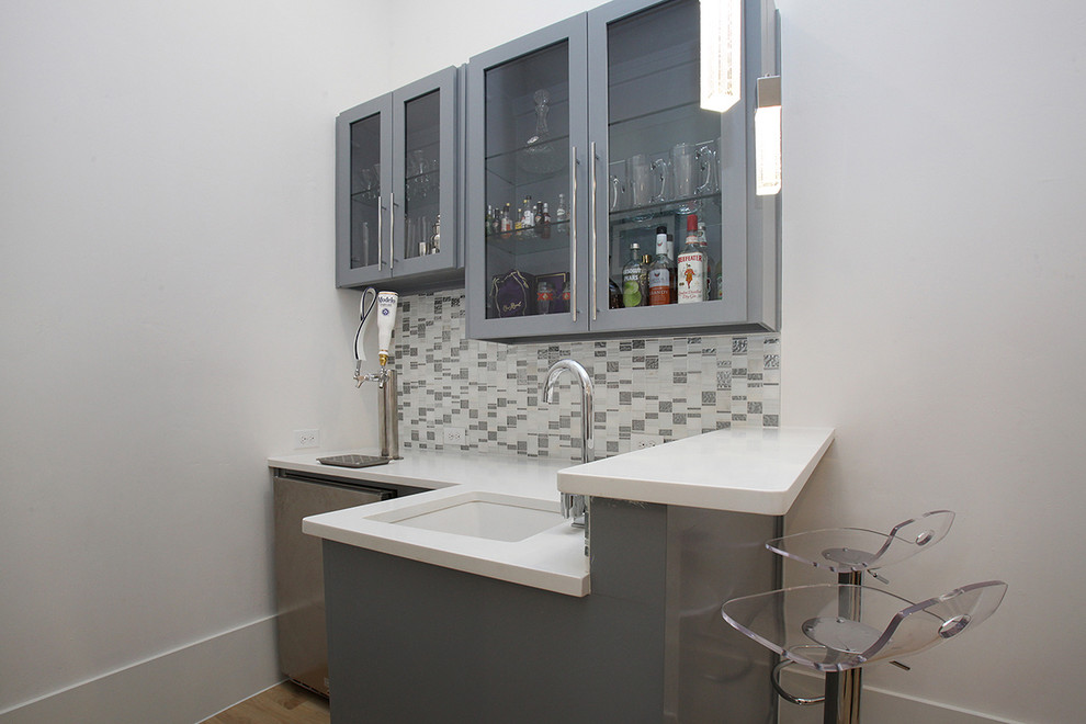 This is an example of a large modern l-shaped wet bar in Dallas with an undermount sink, shaker cabinets, grey cabinets, solid surface benchtops, white splashback, mosaic tile splashback, light hardwood floors and beige floor.