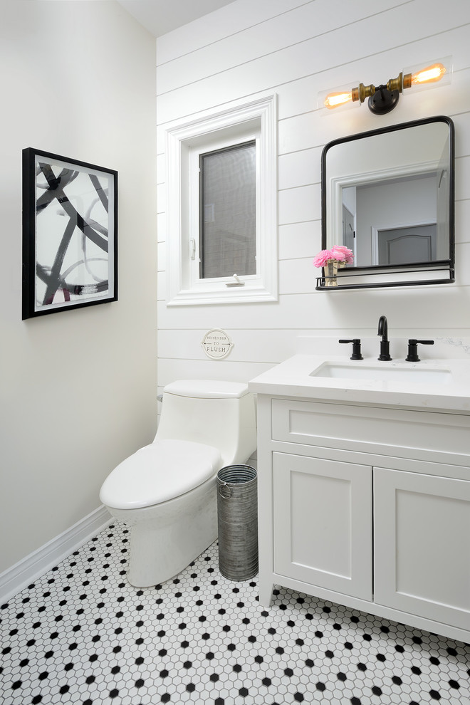 This is an example of a mid-sized country powder room in Toronto with recessed-panel cabinets, white cabinets, a one-piece toilet, white walls, ceramic floors, a drop-in sink, engineered quartz benchtops, multi-coloured floor and white benchtops.