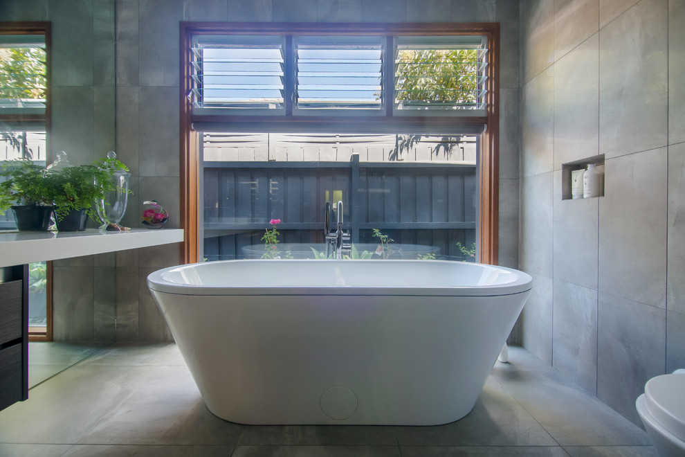 This is an example of a contemporary master bathroom in Melbourne with open cabinets, white cabinets, engineered quartz benchtops, a freestanding tub, an open shower, gray tile and stone tile.